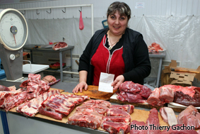 Photo d'une bouchère, derrière son étal au marché montrant son certificat d'origne de la viande.